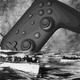 A Stadia controller sinks into a black and white photo of the ocean as people flee on life boats.